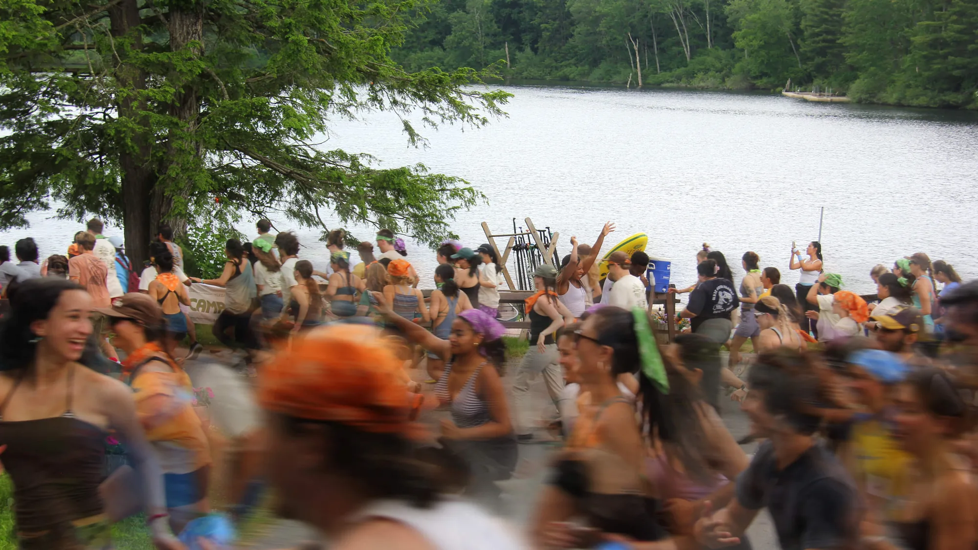 Campers in orange caps and bandanas running by the lake