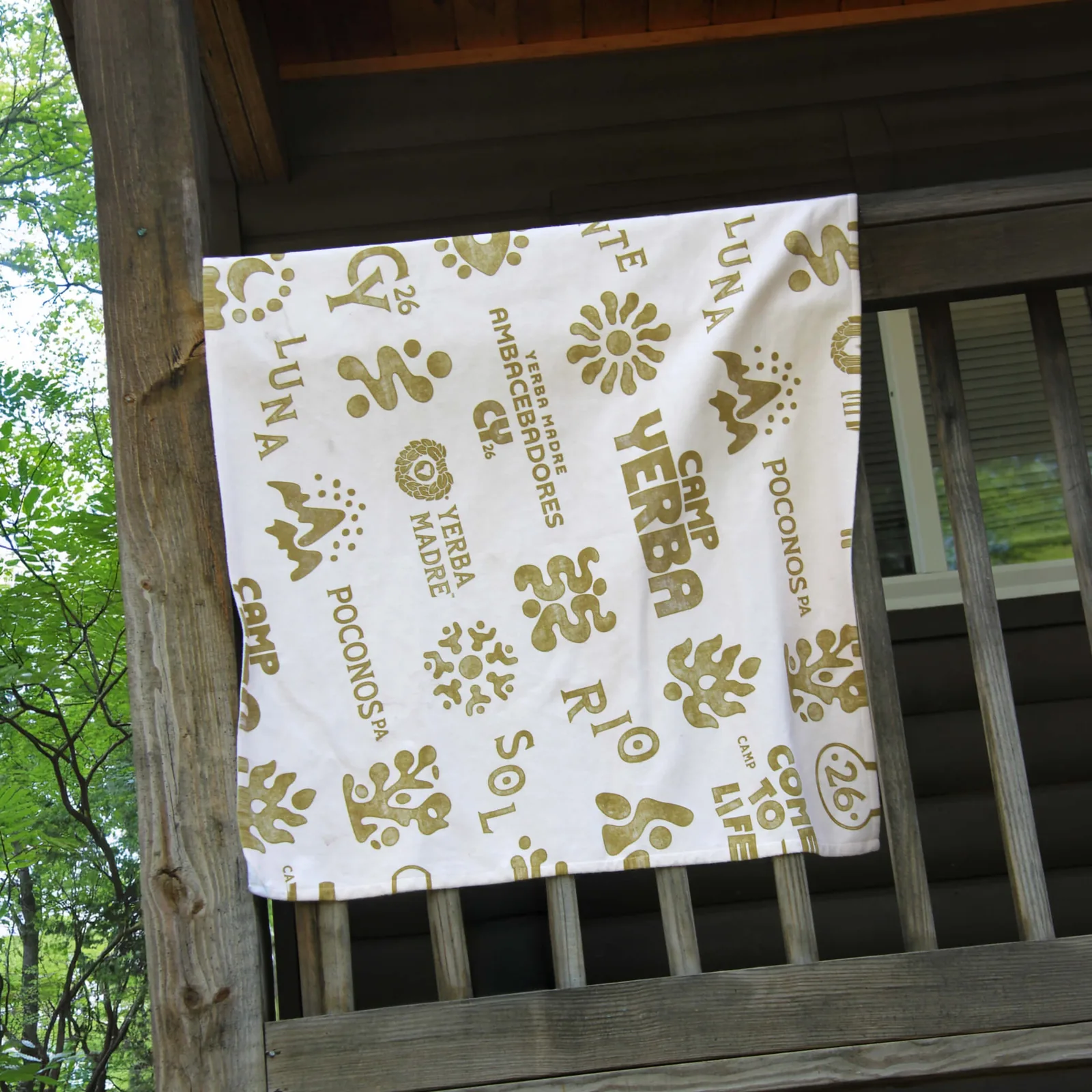 Camp Yerba pattern towel with icons and house names over a cabin railing