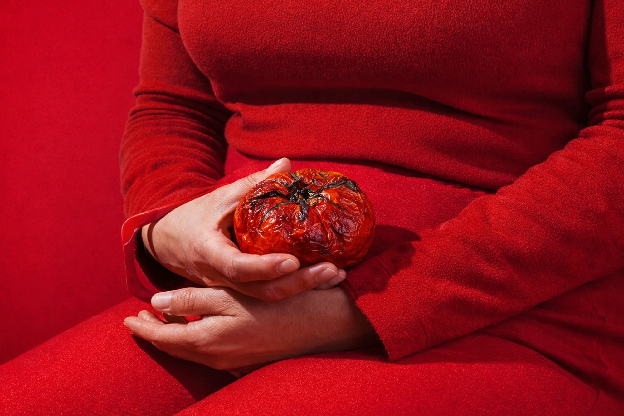 Hands holding a roasted tomato against a red dress